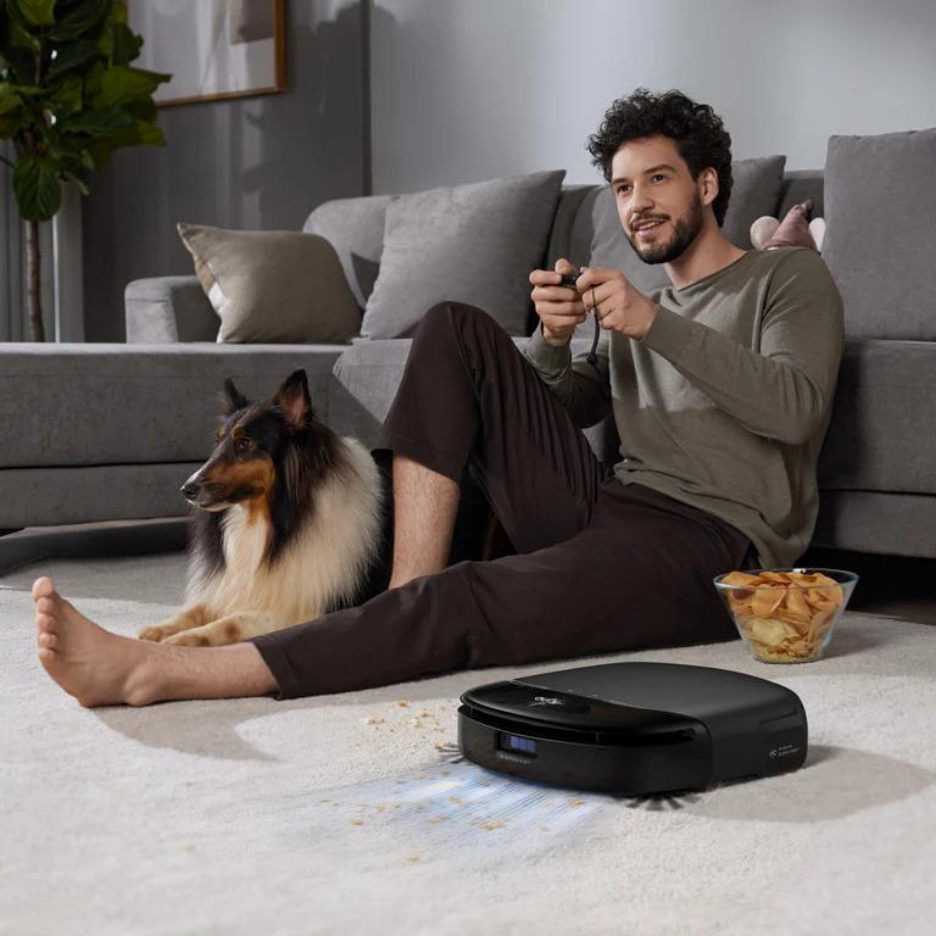 The eufy Omni S1 Pro robot vacuum cleaner vacuums the living room carpet, next to a man and his dog